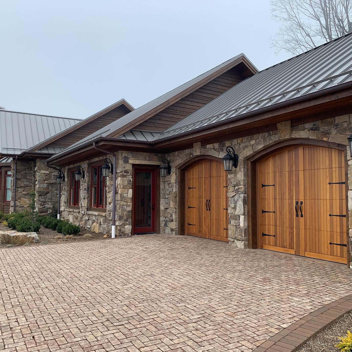 a brick driveway leads to a stone house with wooden garage doors